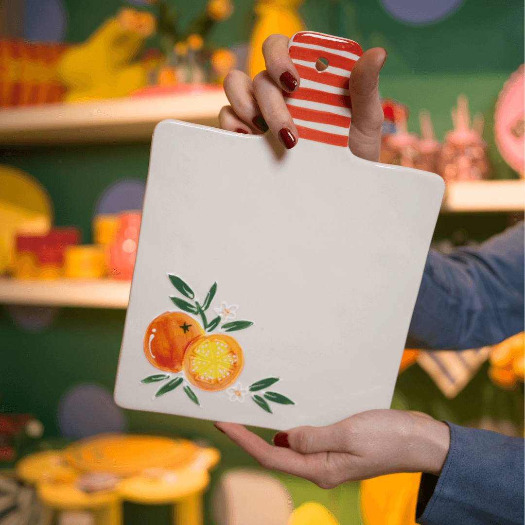Präsentation einer weißen Servierplatte aus Keramik mit rot-weiß gestreiftem Griff und Orangen-Illustration.