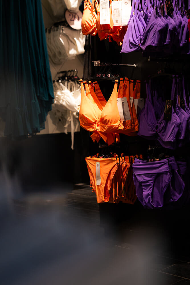 Farbenfrohe Bikinis in leuchtendem Orange und Violett hängen auf Kleiderbügeln an einem Verkaufsständer.