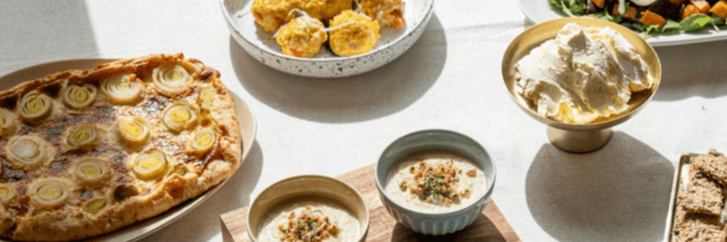 Ein gedeckter Tisch mit verschiedenen winterlichen Gerichten, darunter eine Lauch-Quiche, Suppenschüsseln und eine Schale mit Dips.