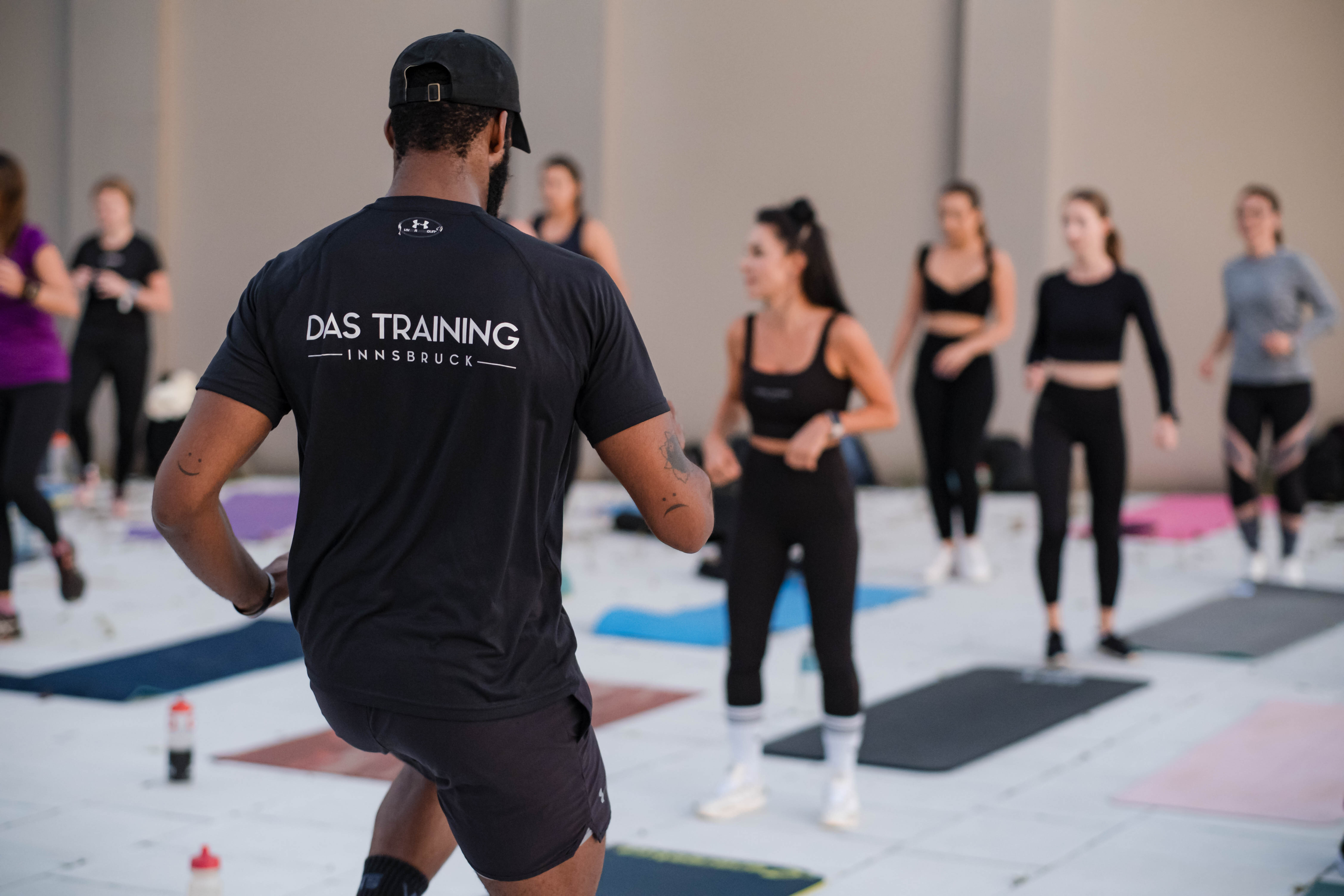 Ein Fitness-Trainer leitet eine Gruppe von Teilnehmenden während eines HIIT-Outdoor-Workouts auf Trainingsmatten an.
