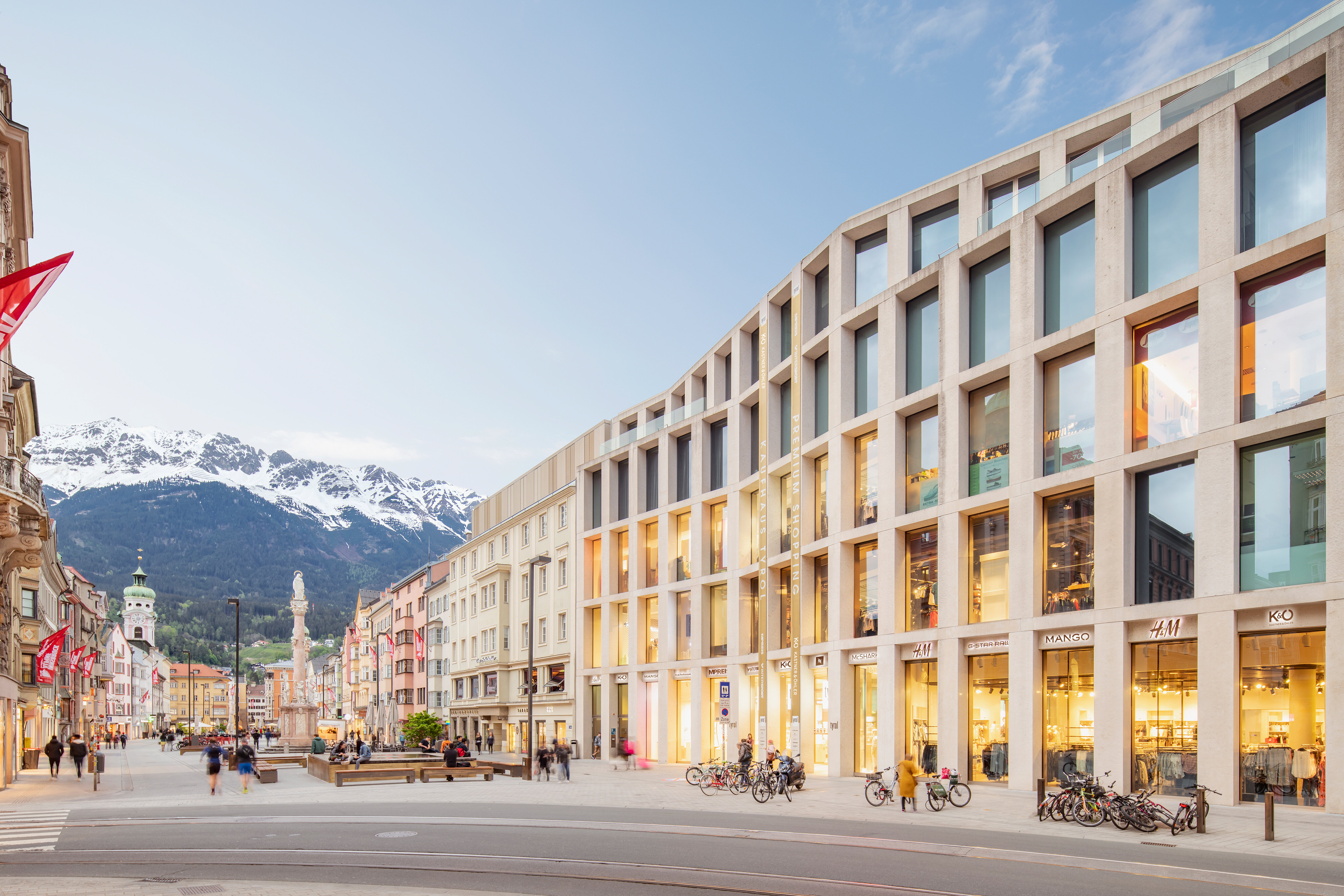 Fassade des Kaufhaus Tyrol mit großen Fensterfronten in der Fußgängerzone der Maria-Theresien-Straße mit der Annasäule und verschneiten Bergen im Hintergrund.