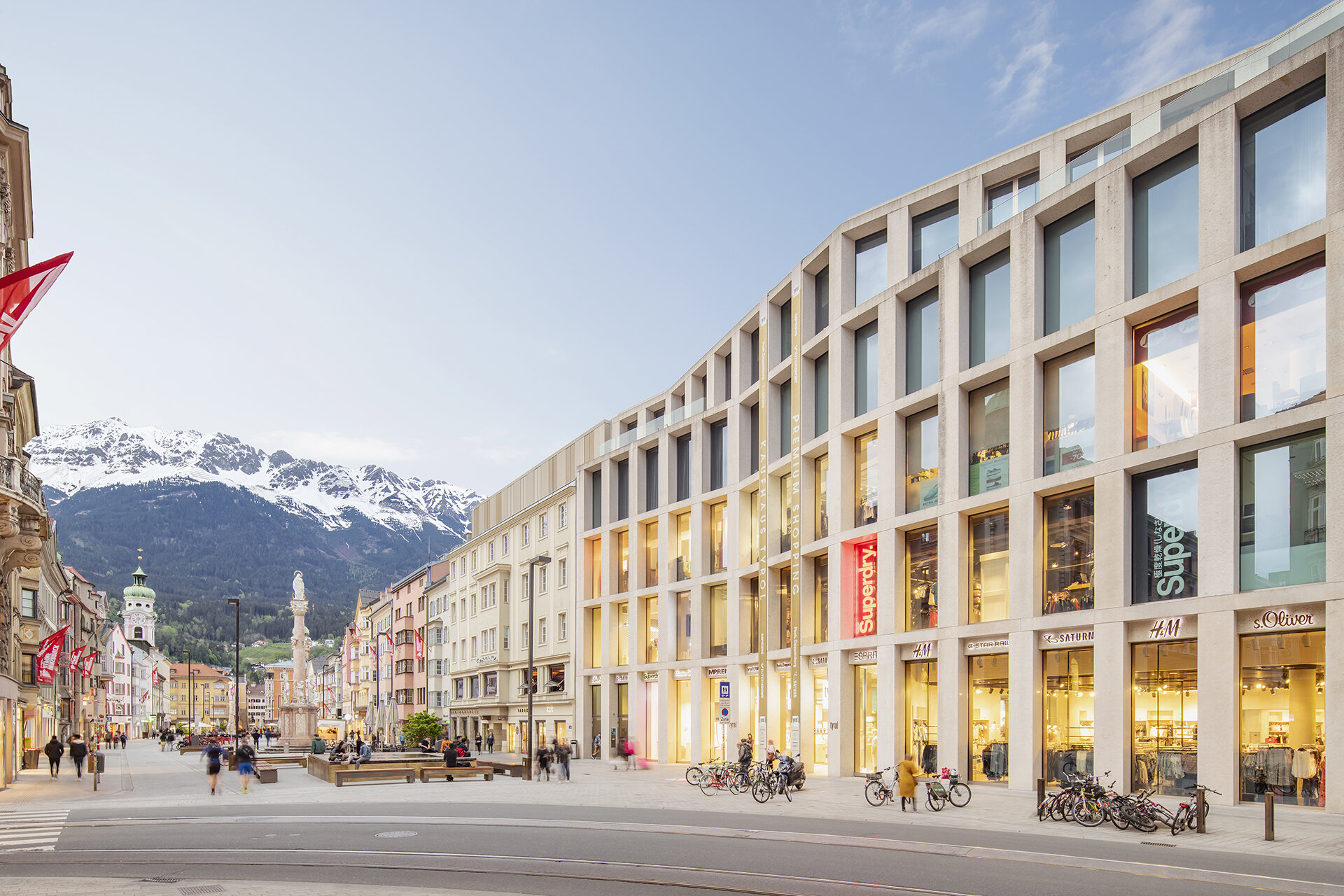 Fassade des Kaufhaus Tyrol mit großen Fensterfronten in der Fußgängerzone der Maria-Theresien-Straße mit der Annasäule und verschneiten Bergen im Hintergrund.