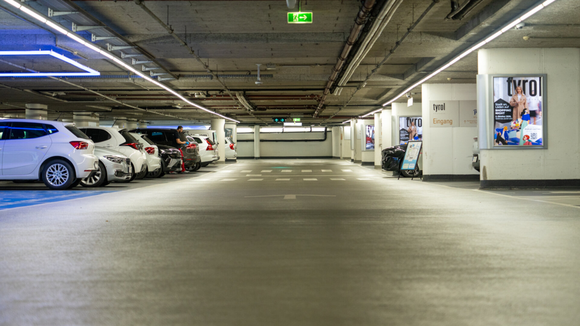 Beleuchtete Tiefgarage des Kaufhaus Tyrol mit geparkten Autos und gut sichtbarer Beschilderung.