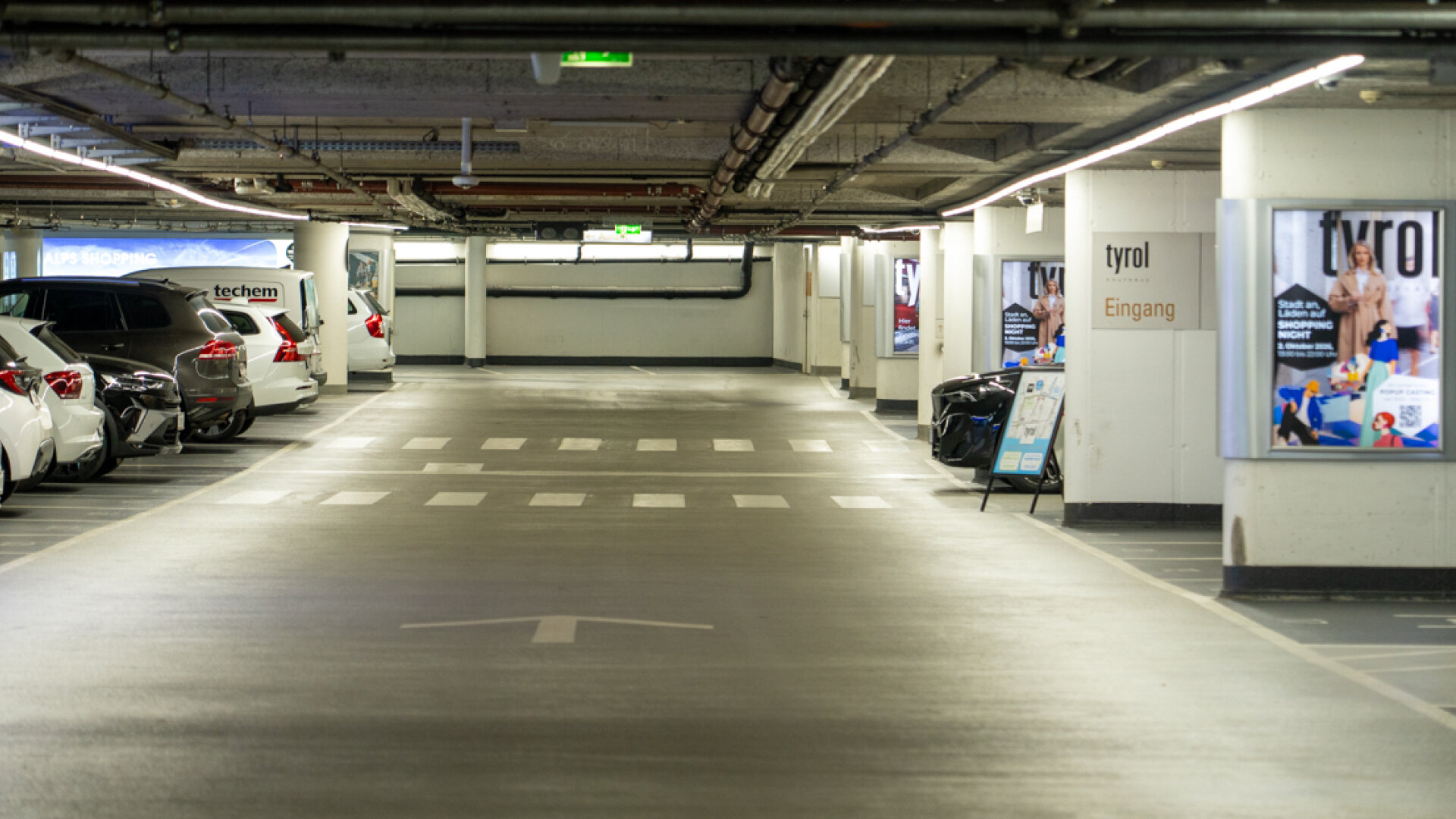 Übersichtlicher Fahrbereich der modernen Kaufhaus-Tyrol-Parkgarage mit ausgewiesener Fußgängerzone und Werbedisplays.