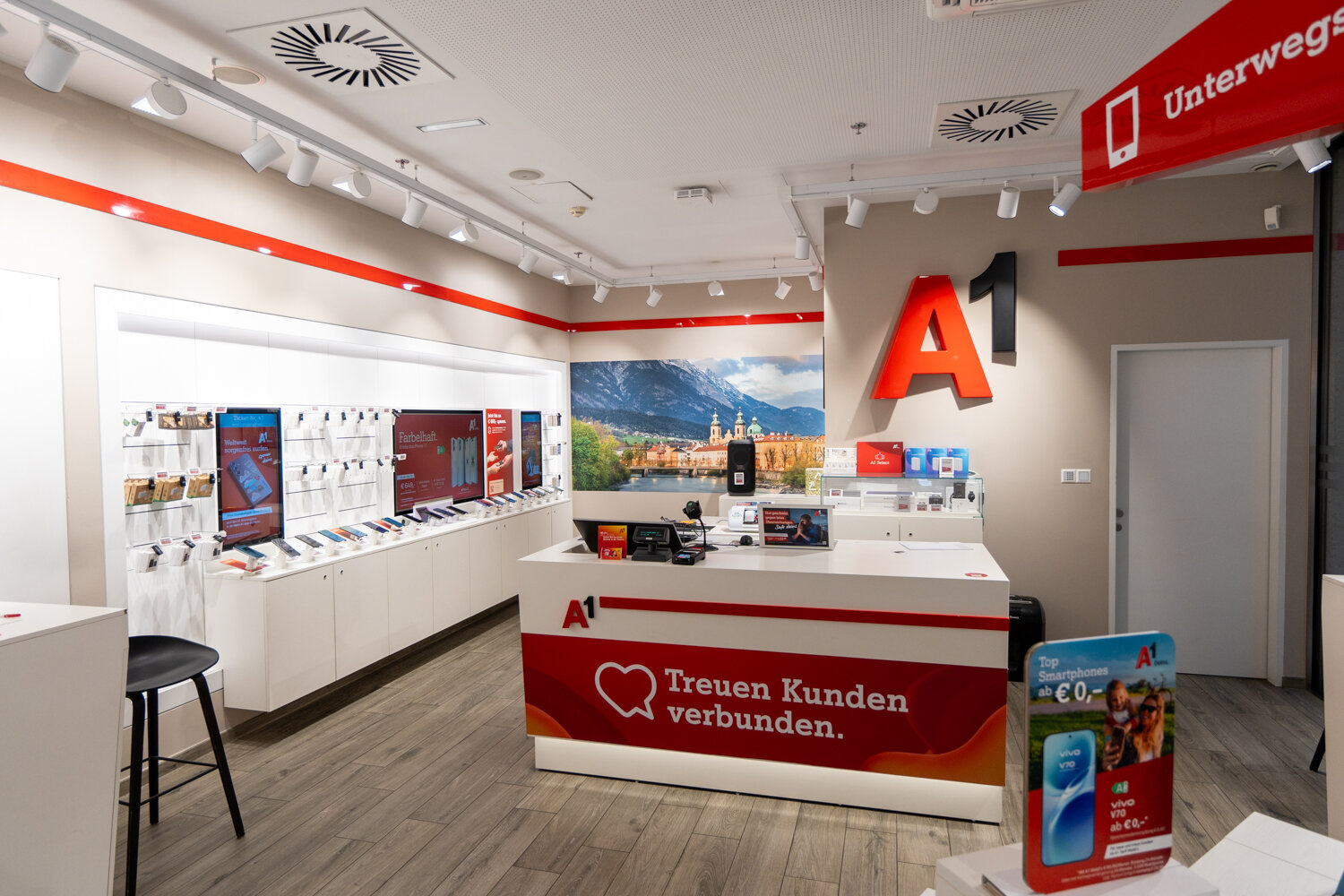Kassen- und Servicebereich im A1 Shop mit weißem Tresen, großem roten 3D-Wandlogo und roten Wegweisern an der Decke.