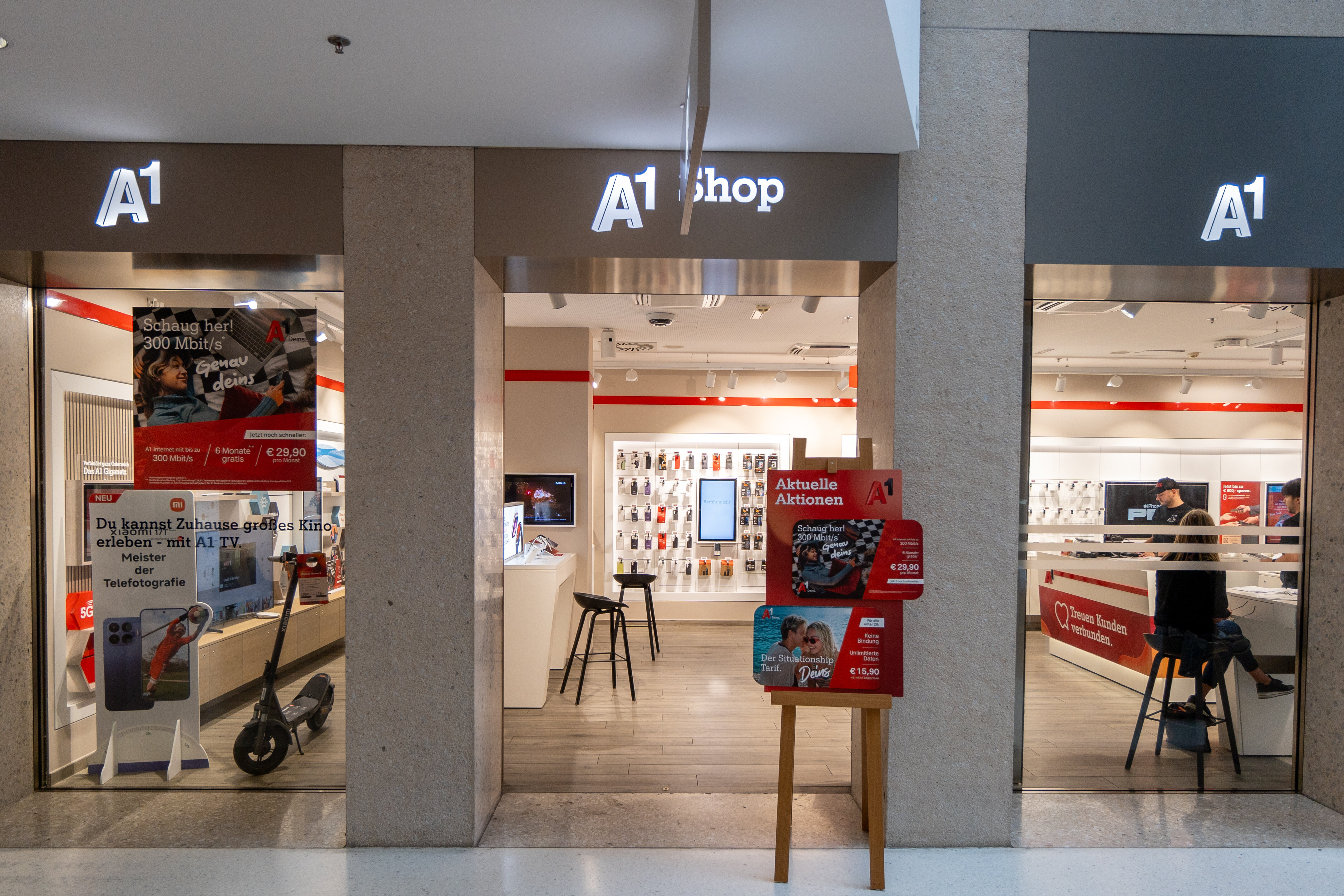 Außenansicht eines A1 Shops mit gläsernem Eingang, beleuchtetem Logo und modernem Verkaufsraum mit Displays.
