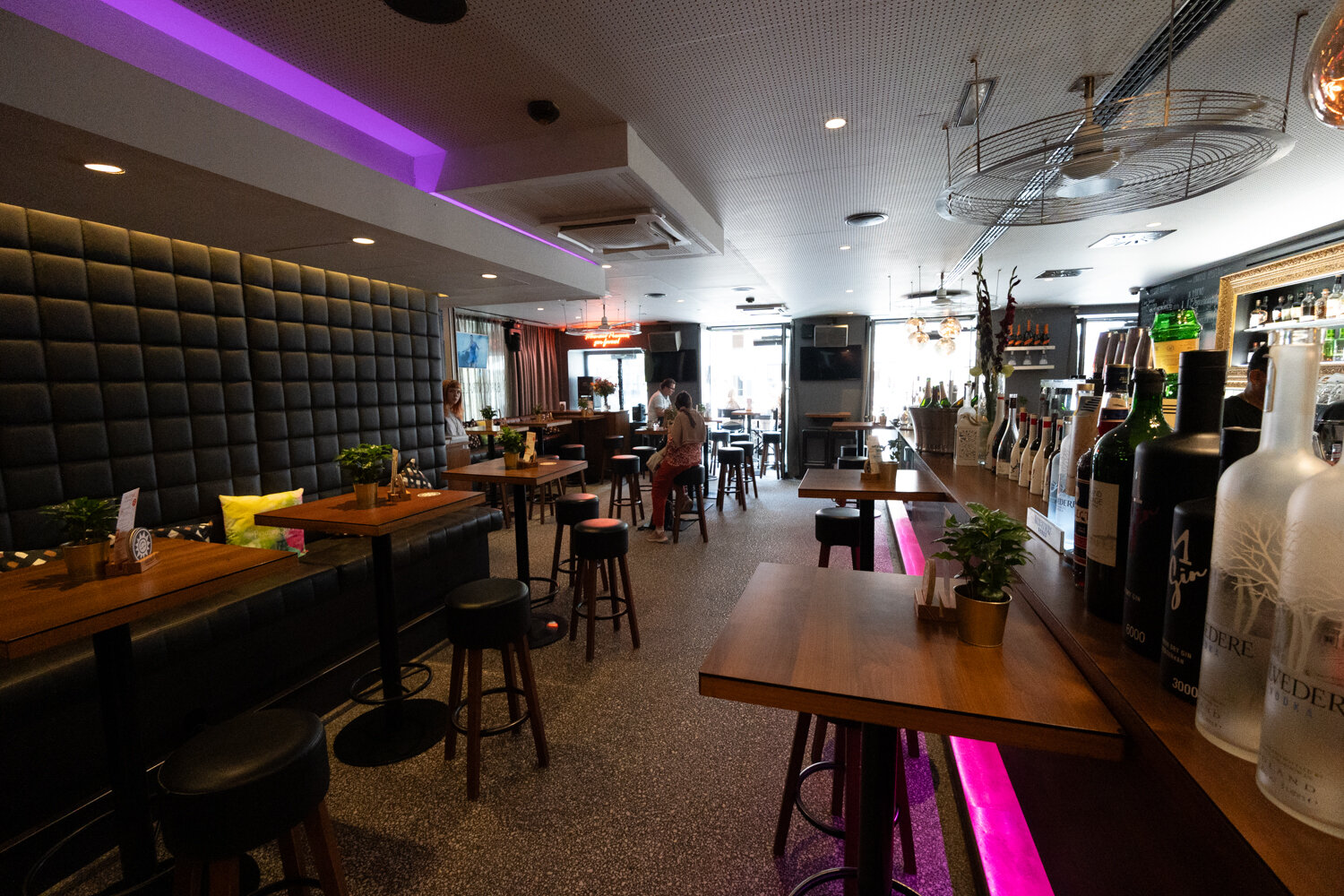 Modern eingerichteter Gastraum der Bar Centrale mit dunkler Polsterbank, Stehtischen und violettem LED-Licht.