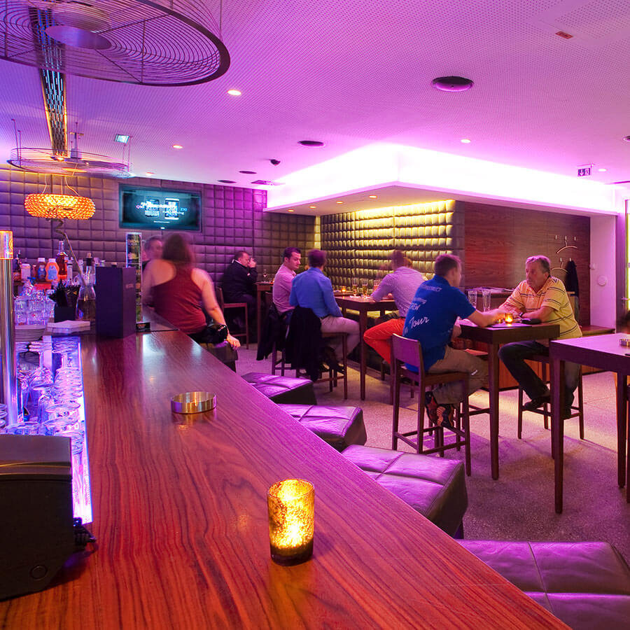Stilechter Innenbereich der Bar Centrale mit langer Holztheke, Lederhockern und stimmungsvoller, violetter LED-Beleuchtung.