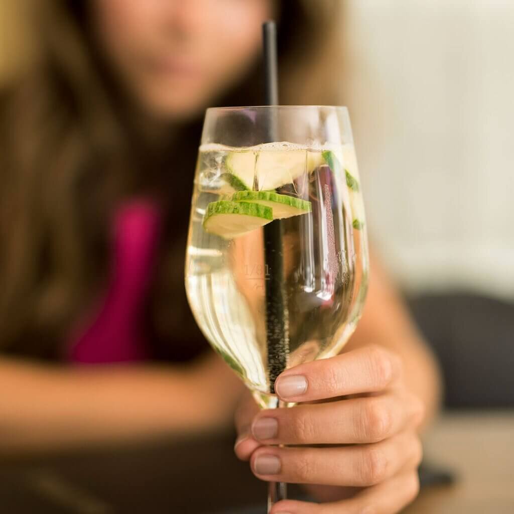 Ein erfrischender Cocktail im Weinglas, garniert mit knackigen Gurkenscheiben und einem schwarzen Strohhalm.