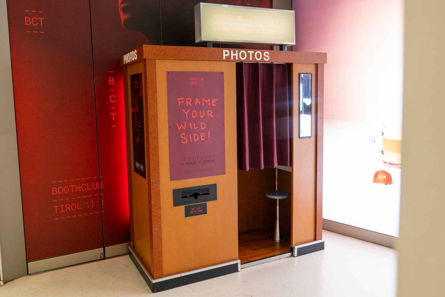 Fotoautomat im Retro-Holzdesign mit dunklem Vorhang und Plakat mit der Aufschrift „Frame Your Wild Side!“.