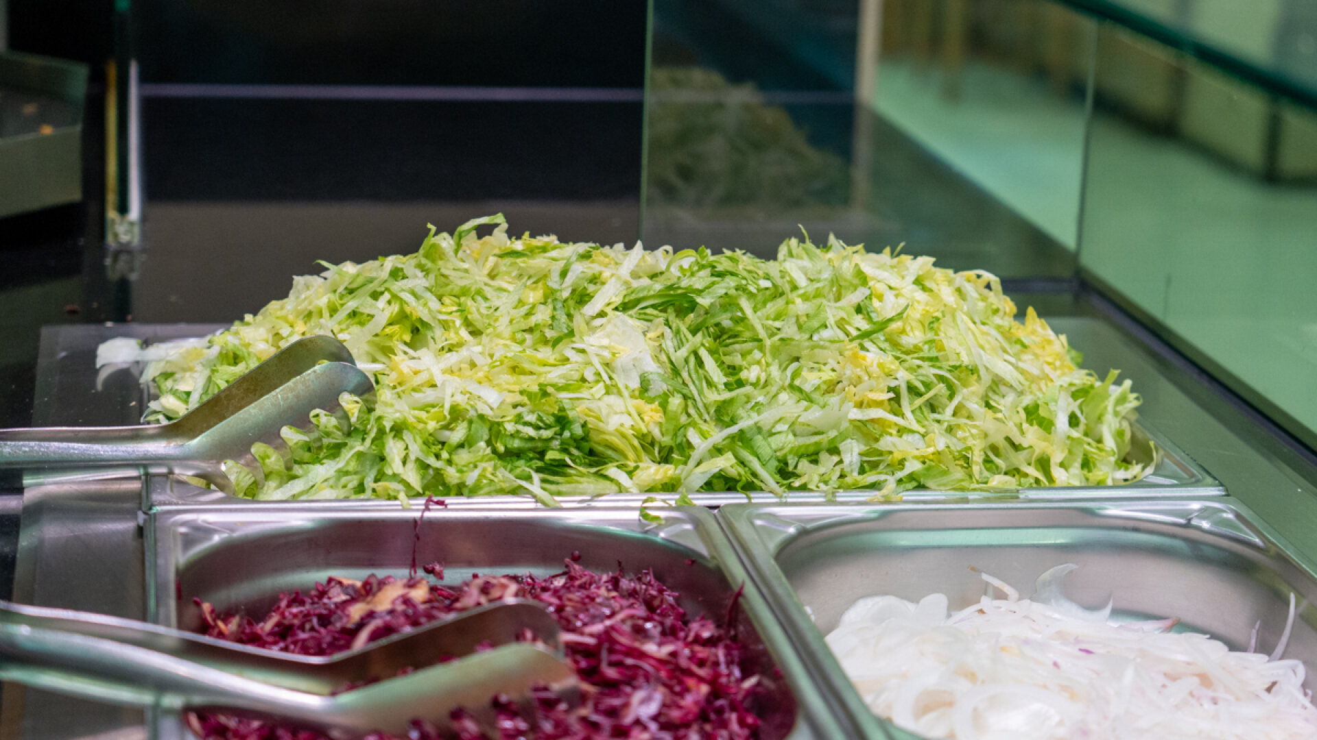Edelstahl-Gastrobehälter gefüllt mit frisch geschnittenem Eisbergsalat, Rotkraut und Zwiebeln an einer Salatbar bei Cütkos