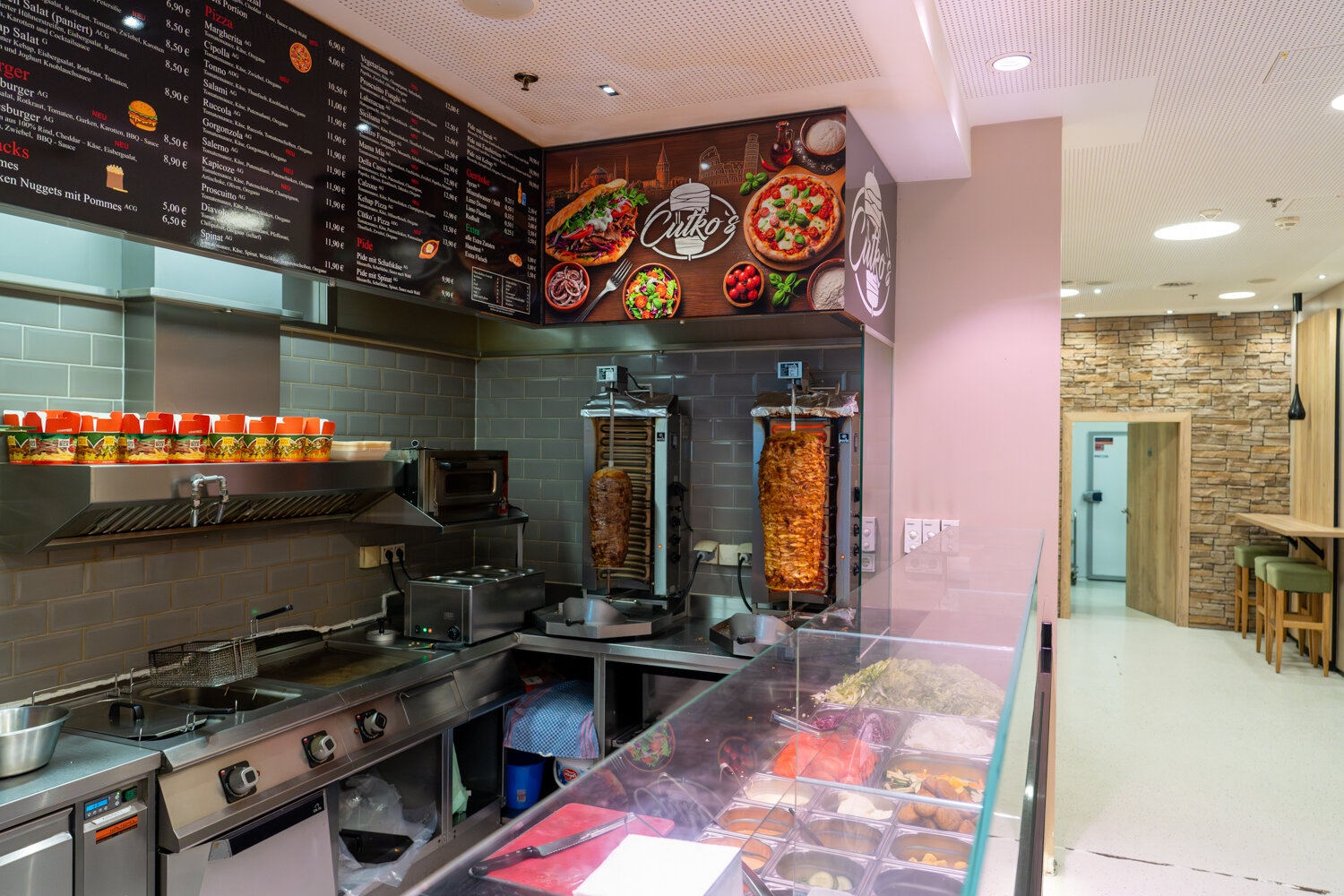 Blick in die Küche von Cütko’s mit zwei Döner-Spießen, Fritteusen, digitaler Menükarte und der Theke.