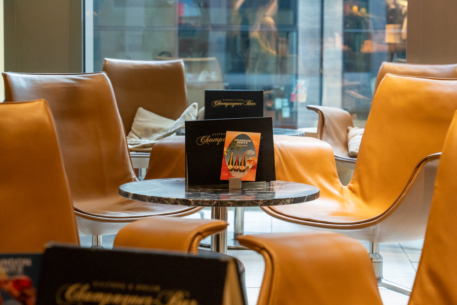 Braune Leder-Lounge-Sessel um einen kleinen Marmortisch mit Aufstellern der Champagner-Bar.