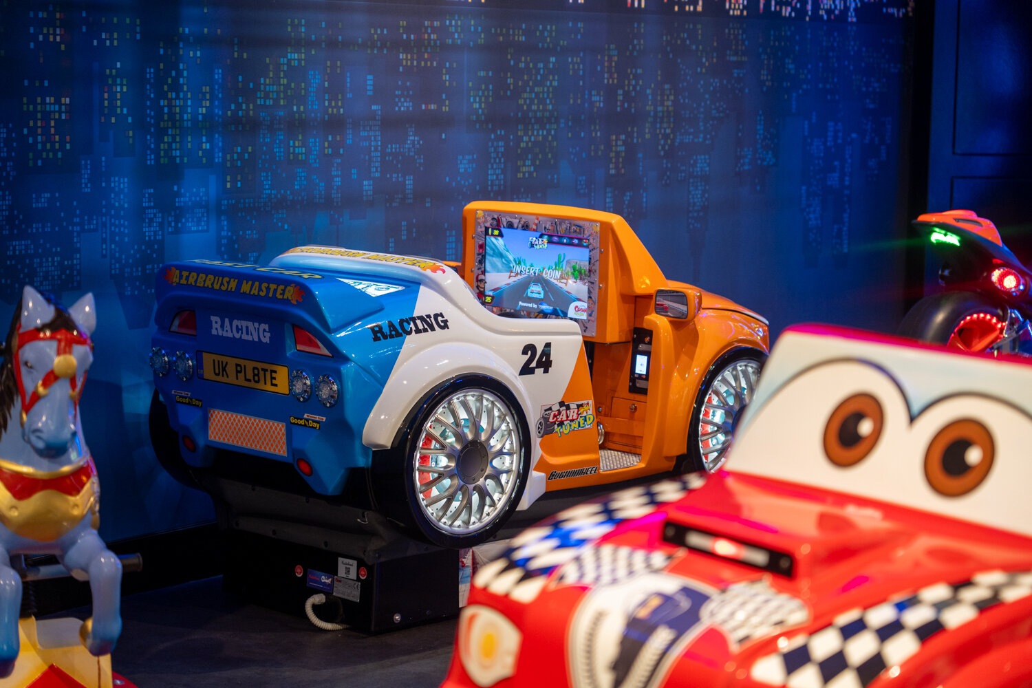 Bunte Kinder-Rennauto-Fahrgeschäfte mit kleinen Bildschirmen vor einer dunkelblauen Wand.