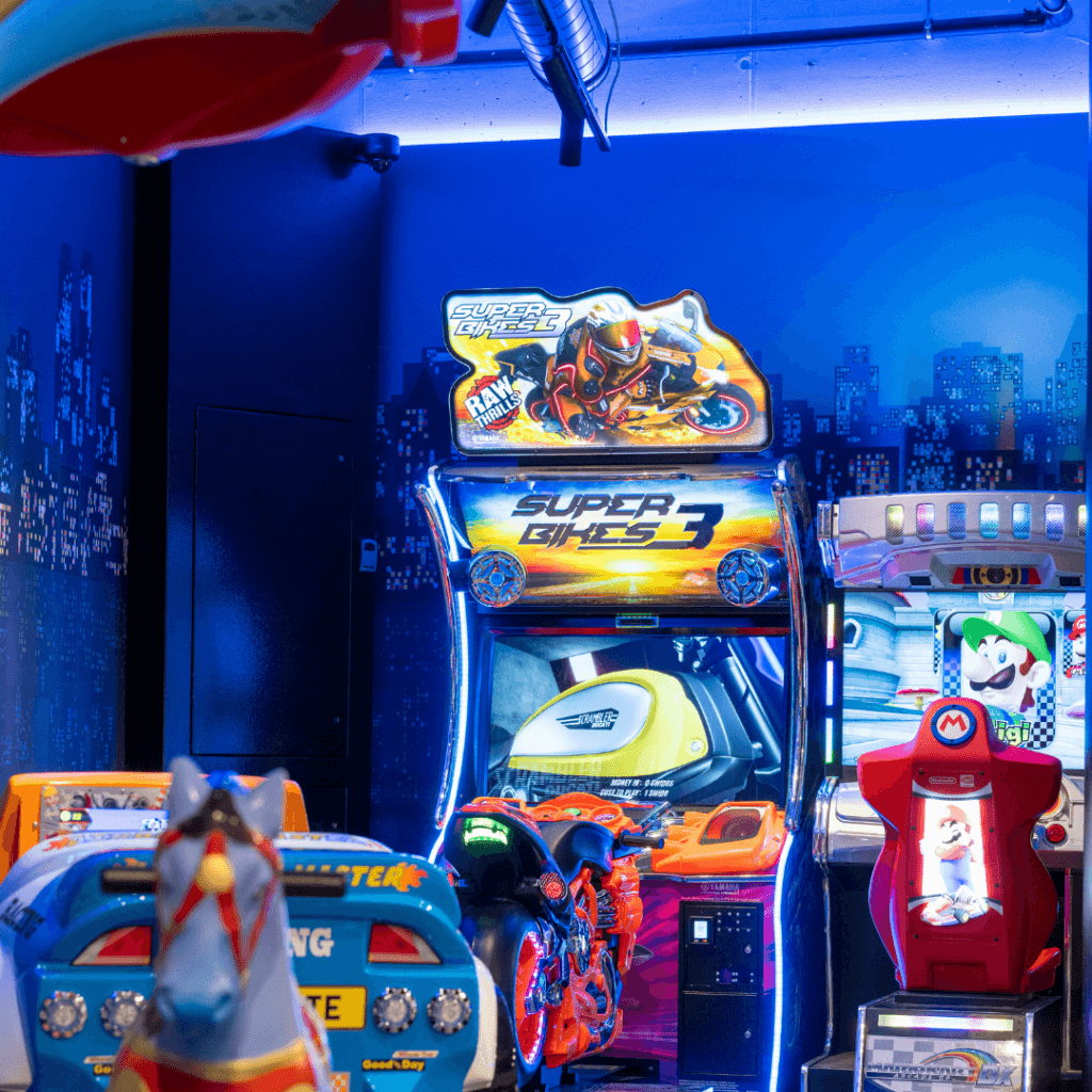 Der Rennspielautomat „Super Bikes 3“ mit Motorrad-Controller neben einem Nintendo-Spielautomaten unter blauem Licht.