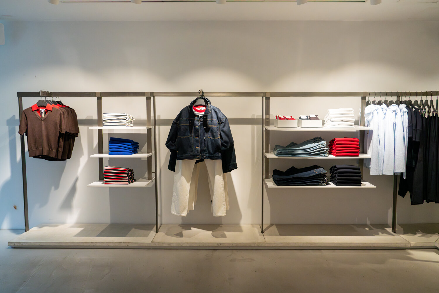 Geordnete Wandpräsentation bei COS mit hängenden Oberteilen, Jeans und ordentlich gefalteten Kleidungsstücken.