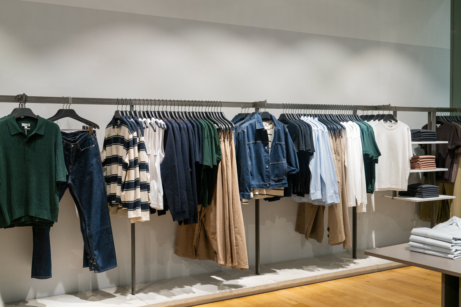 Minimalistische Kleiderstange bei COS mit sortierten Hemden, Shirts, Jeans und Jacken in gedeckten Farben.