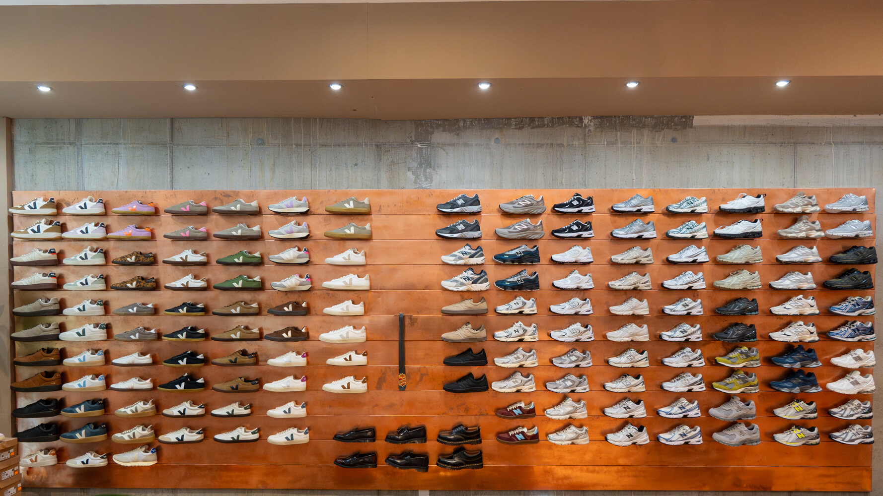 Große Sneaker-Wand auf Kupferhintergrund mit zahlreichen Sportschuhen und Alltagsschuhen verschiedener Farben sortiert im Cuprum 29 Store.