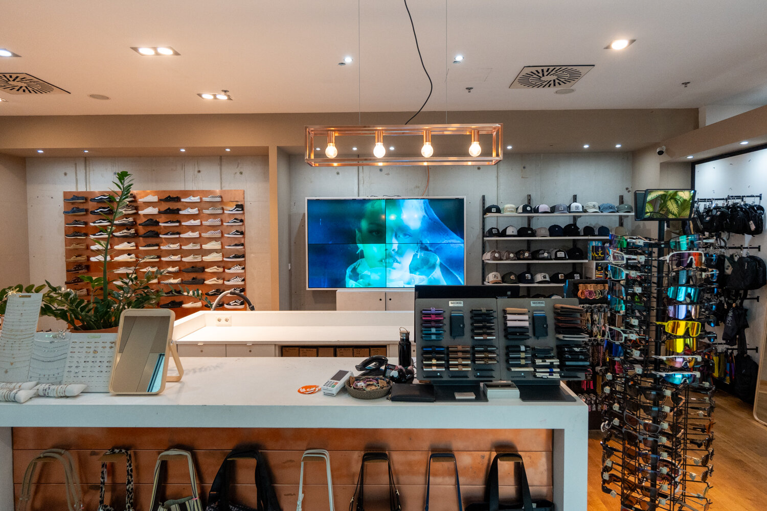 Kassenbereich bei Cuprum29 mit weißer Verkaufstheke Display-Wand für Brillen Geldbörsen-Ständer Sneakers an der Wand und Screen im Hintergrund.