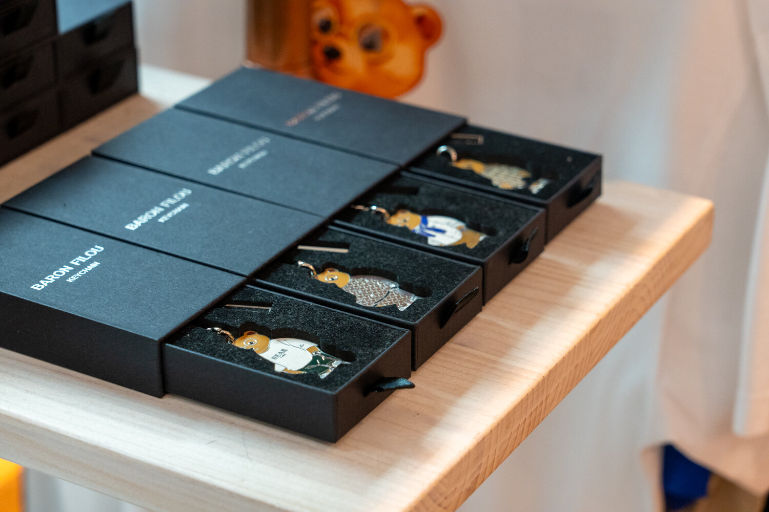 Schwarze Geschenkverpackungen der Marke Baron Filou mit geöffneten Schubladen, die Bären-Schlüsselanhänger auf Samt präsentieren.