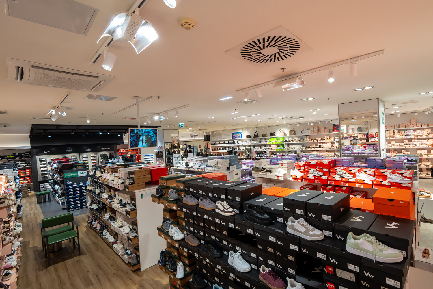 Weitwinkel-Blick in die Deichmann Filiale mit zahlreichen Regalreihen aufgestapelten Schuhkartons Sneakern bekannter Marken und moderner Deckenbeleuchtung.