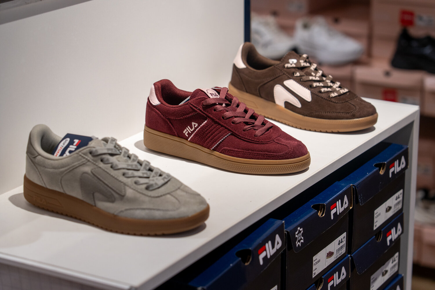 Nahaufnahme von Fila-Sneakern in braun, grau und bordeauxrot auf einem Verkaufsregal bei Deichmann.