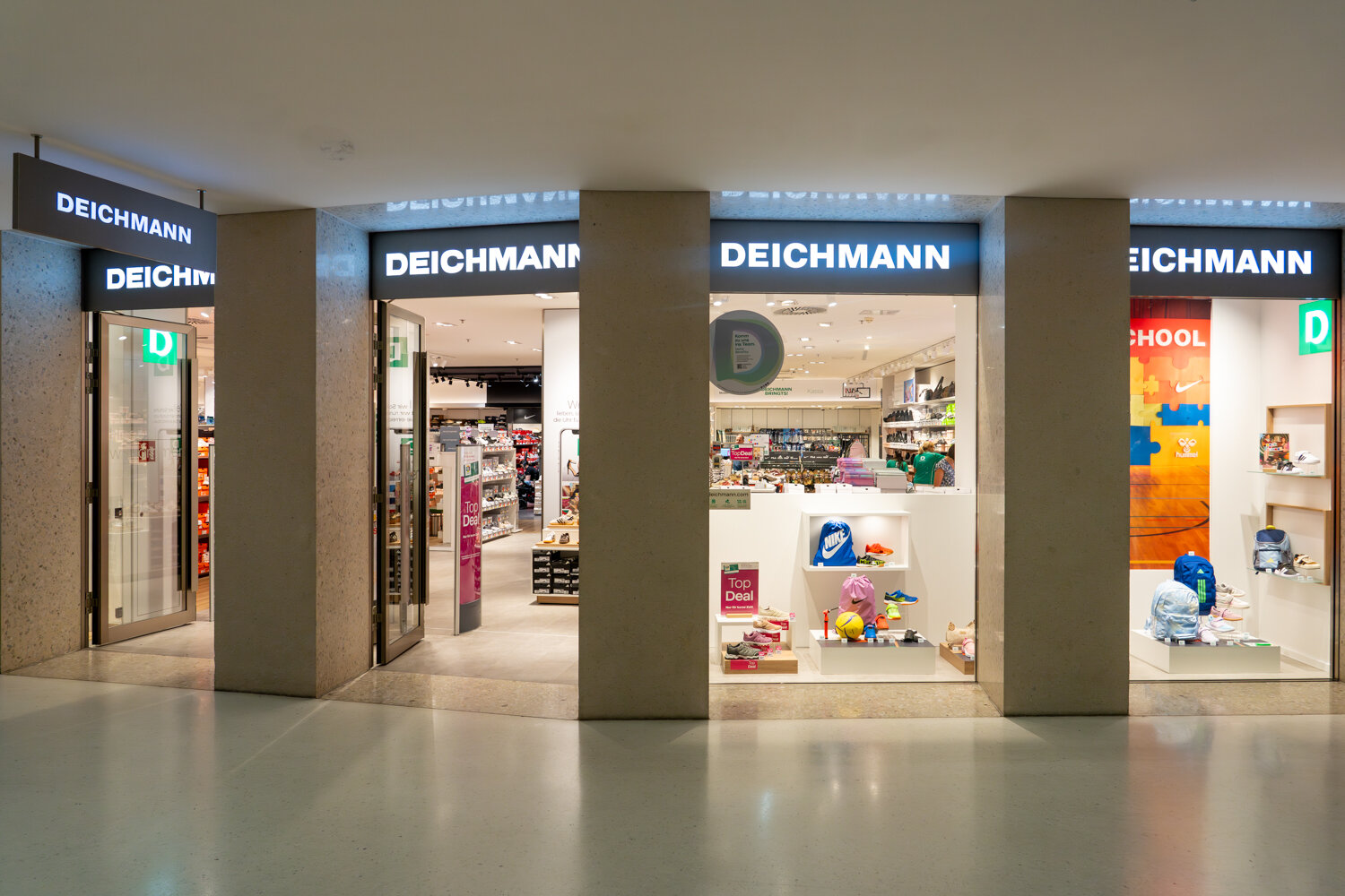Schaufensterfront und Eingangsbereich einer Deichmann-Filiale im Einkaufszentrum mit beleuchtetem Logo und aktuellen Angeboten.