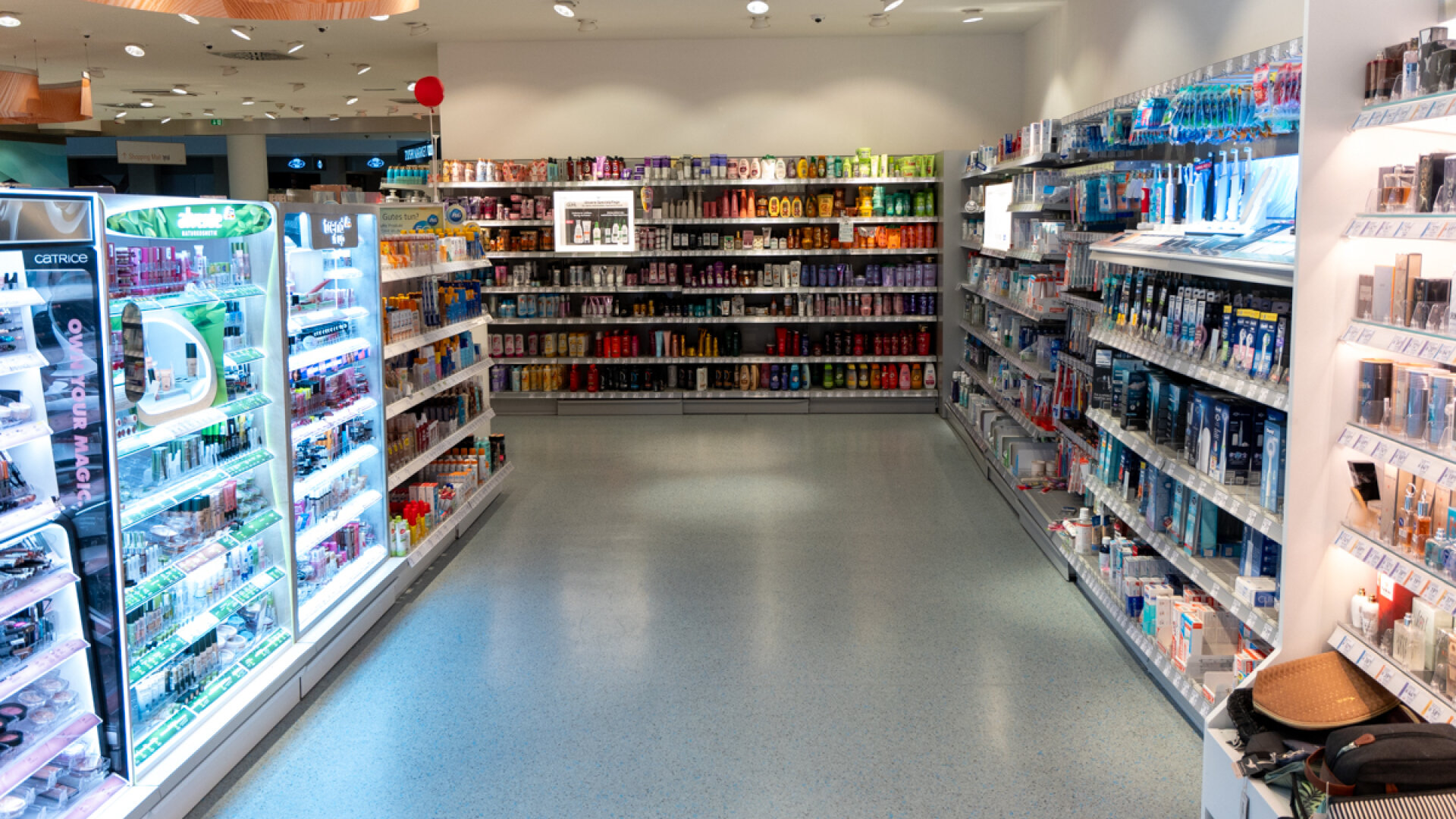Aufgeräumter Gang im dm-Drogeriemarkt mit beleuchteten Regalen für Make-up, Körperpflege und Mundhygiene.