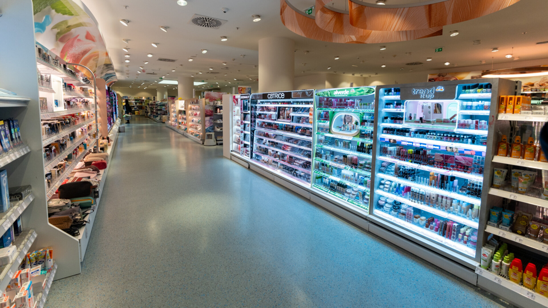 Blick durch die Verkaufsfläche des dm-Marktes mit beleuchteten Make-up-Displays beliebter Kosmetikmarken.