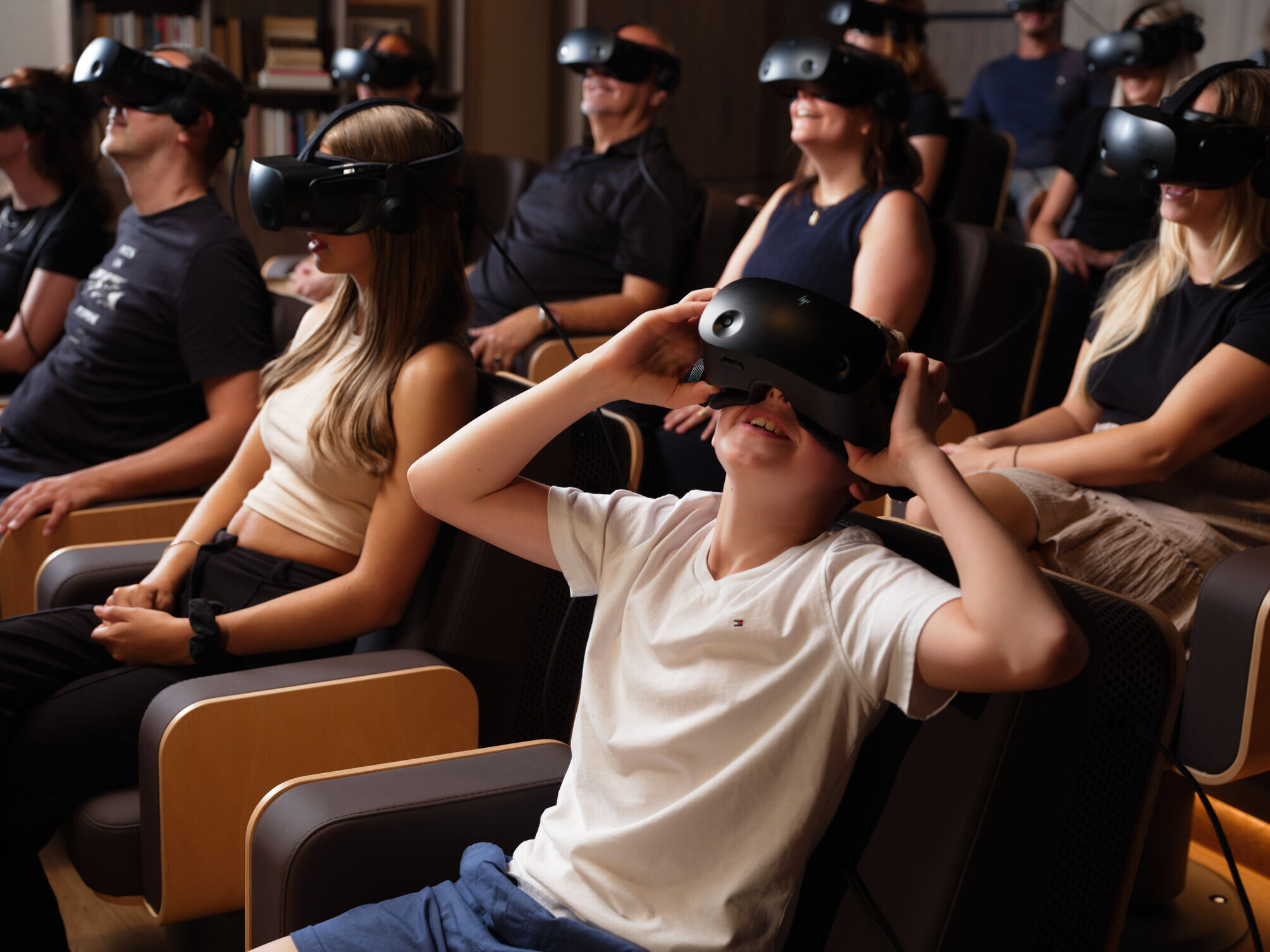 Besucher in Sesseln tragen VR-Headsets und schauen fasziniert nach oben während einer virtuellen Tour.
