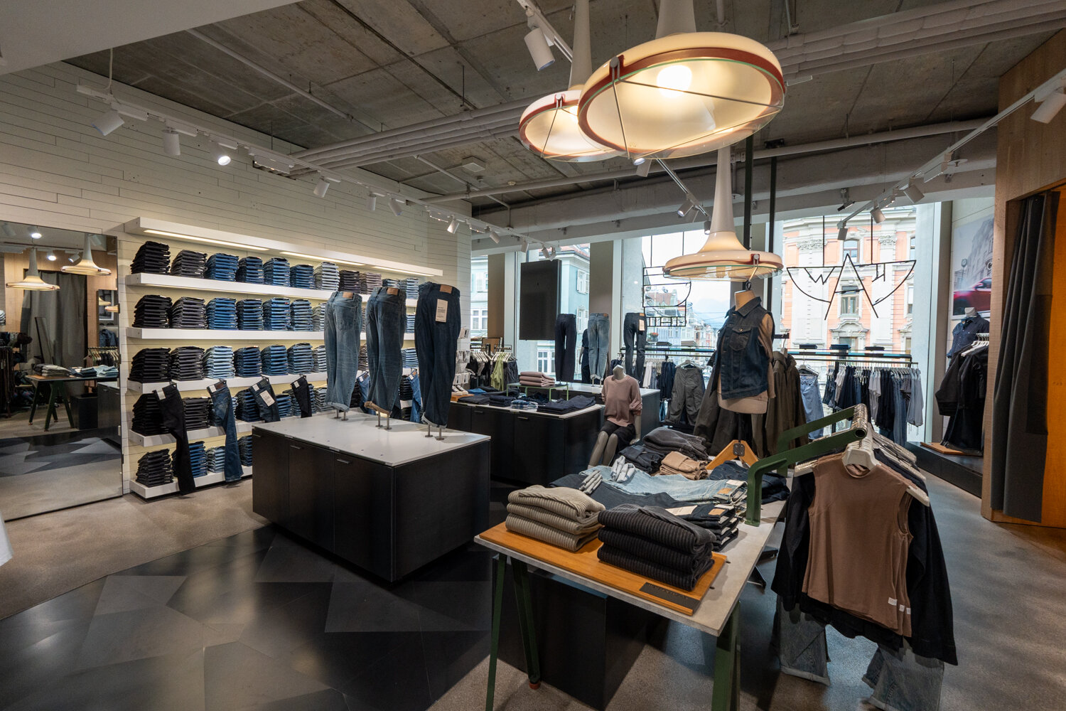 Innenansicht des G-Star RAW Stores mit großer Jeans-Regalwand Präsentationstischen mit Pullovern, Schaufensterpuppen und auffälligen Designer-Lampen.