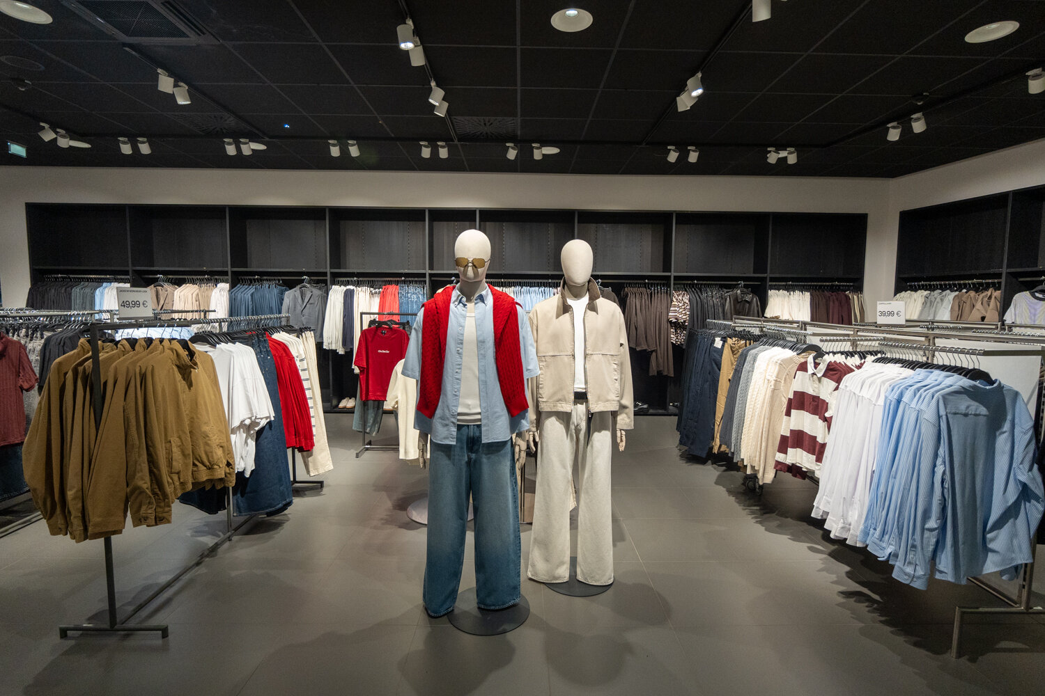 Zwei Schaufensterpuppen im H&M-Store inmitten von Kleiderständern mit Shirts, Jacken und Jeans.