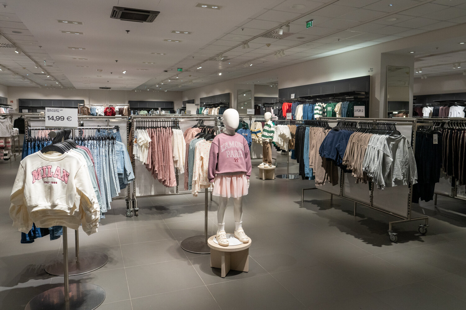 H&M-Kinderabteilung mit Kinder-Schaufensterpuppen, Pullovern und Hosen auf Rollständern.