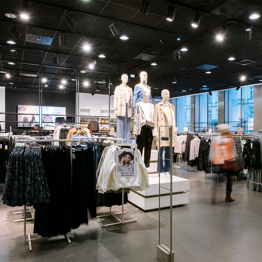 Übersichtliche Damenabteilung bei H&M mit Schaufensterpuppen in herbstlichen Looks und zahlreichen Kleiderständern unter moderner Deckenbeleuchtung.