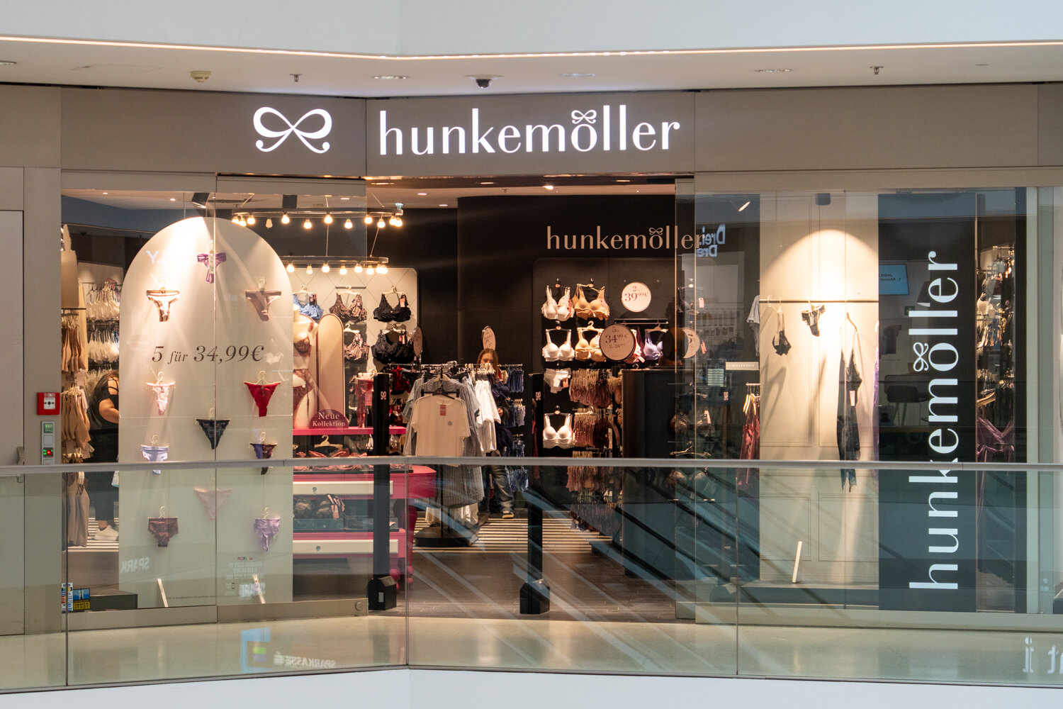 Frontansicht der Hunkemöller-Filiale im Einkaufszentrum mit Glasfront, beleuchtetem Logo und Angebotsschildern.