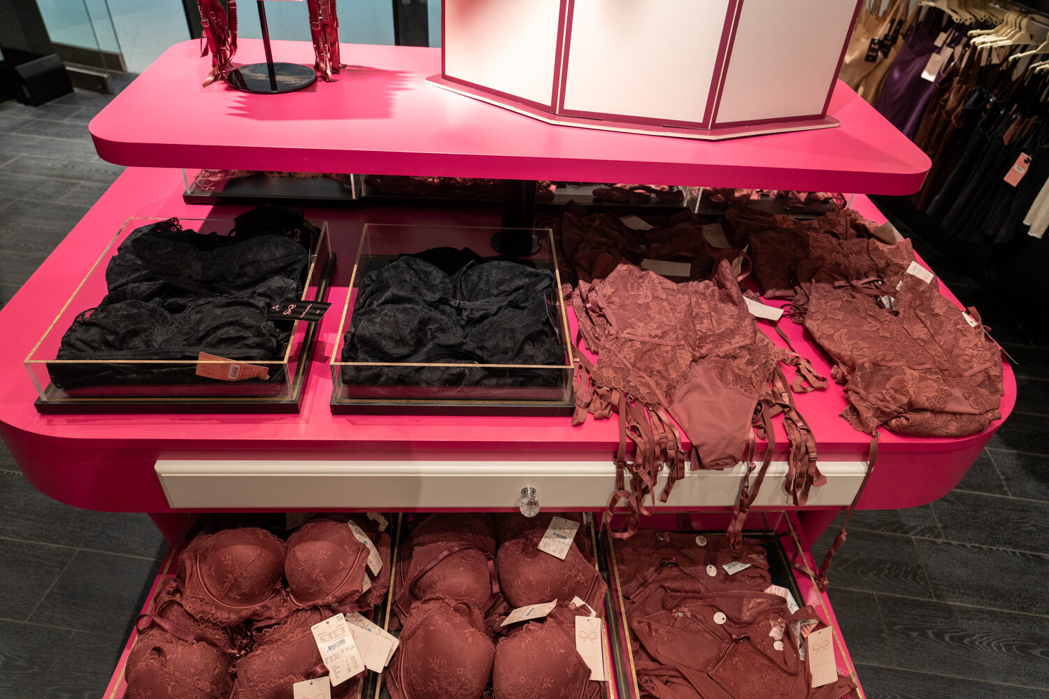Pinker Präsentationstisch bei Hunkemöller mit dunkelroter und schwarzer Lingerie, BHS und Corsagen.