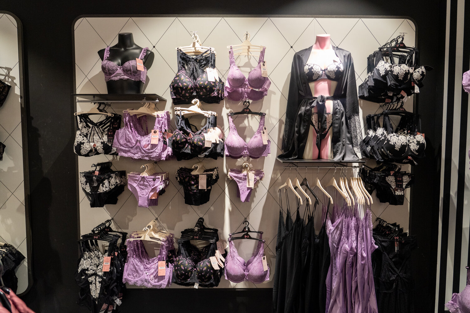 Wandpräsentation bei Hunkemöller mit lila und schwarzer Spitzenunterwäsche, BHS, Slips und einem Seidenmantel auf einer Schaufensterpuppe.
