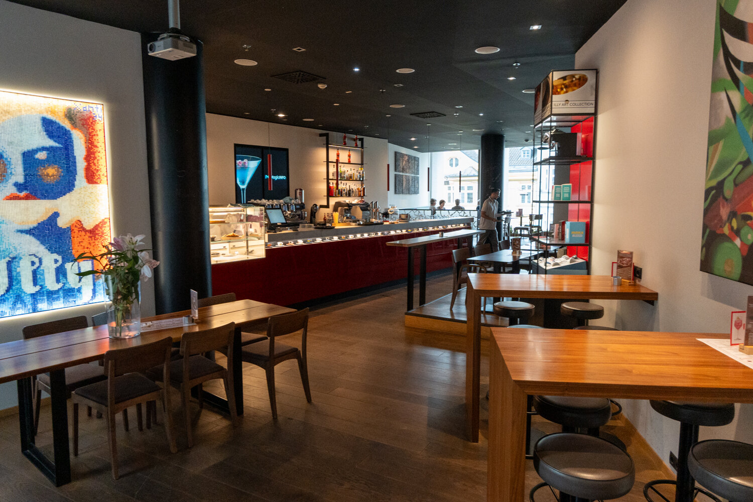Gemütlicher Innenbereich von Illy Caffè mit Tischen, Barhockern, Bar-Theke und bunter Wandkunst.