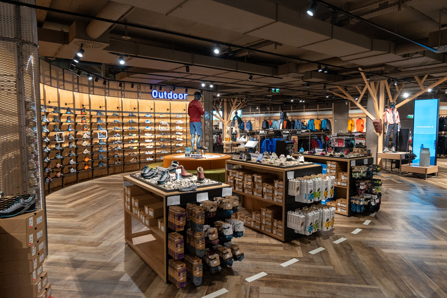 Intersport Outdoor-Abteilung mit Wanderschuh-Regalwand und Holzmöbeln.