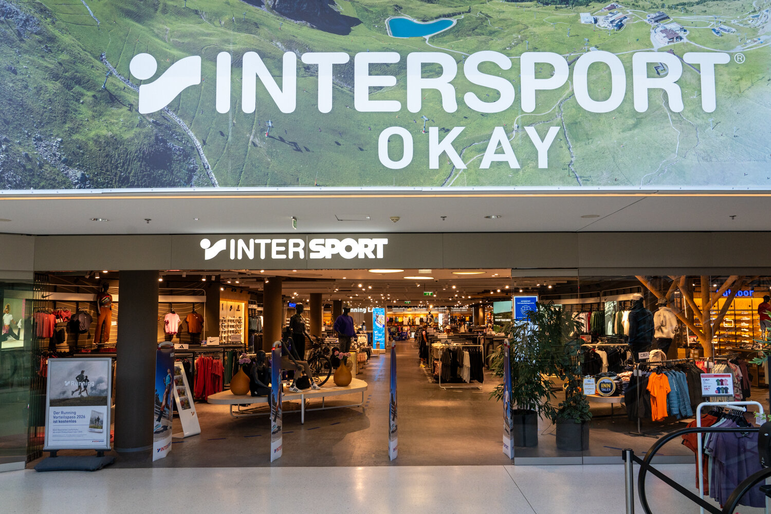 Großzügiger Eingangsbereich der Intersport Okay Filiale mit beleuchtetem Markenlogo und Blick in den Sportfachmarkt.