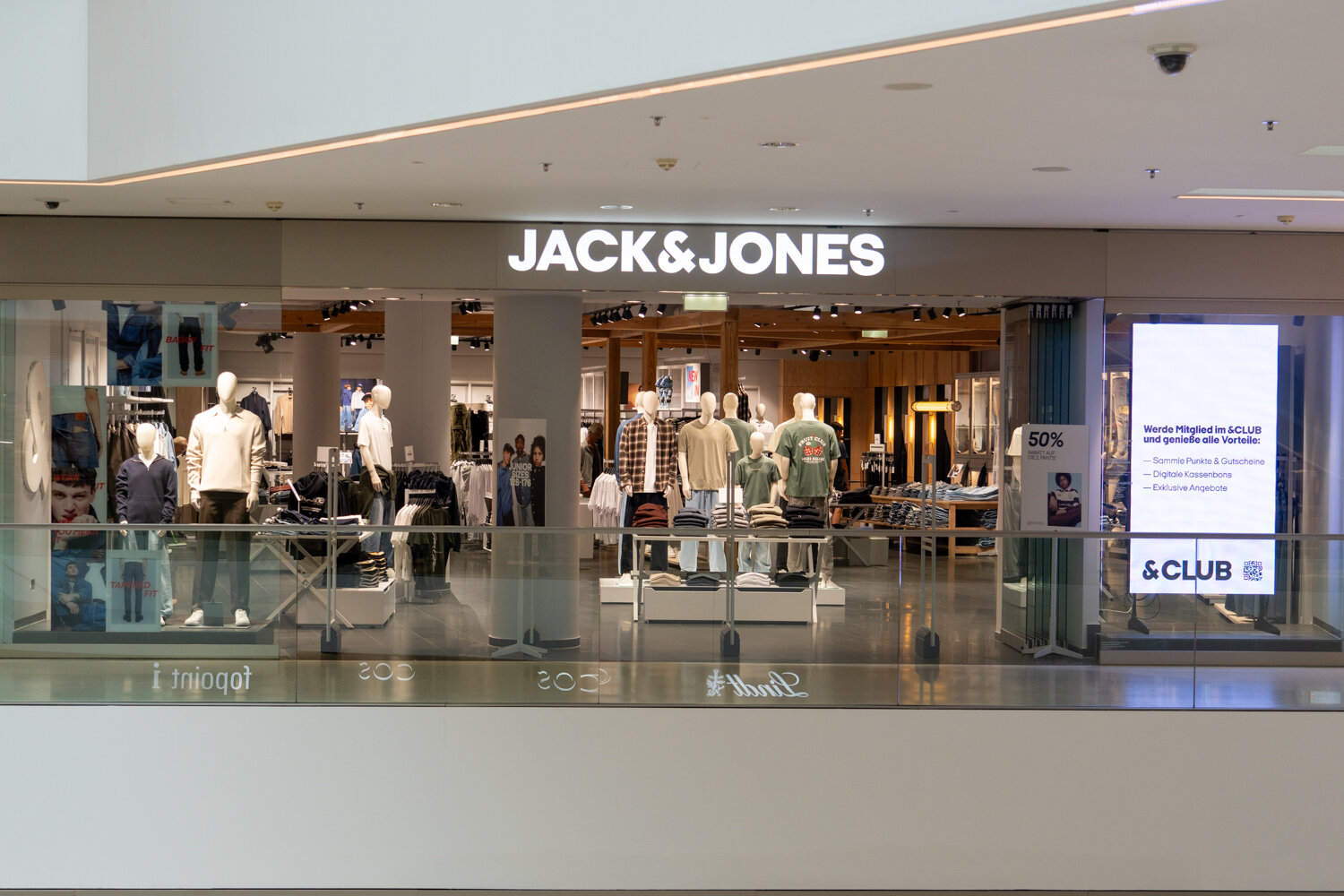 Frontalansicht der Jack & Jones Filiale mit leuchtendem Markenlogo und Schaufensterpuppen in Herrenbekleidung.