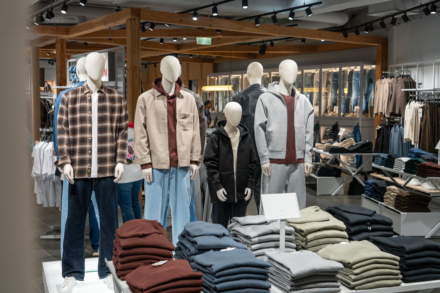 Schaufensterpuppen in einem Jack & Jones Store mit Freizeitbekleidung wie Karohemden, Sweatjacken und Pullover-Stapeln auf einem Tisch.