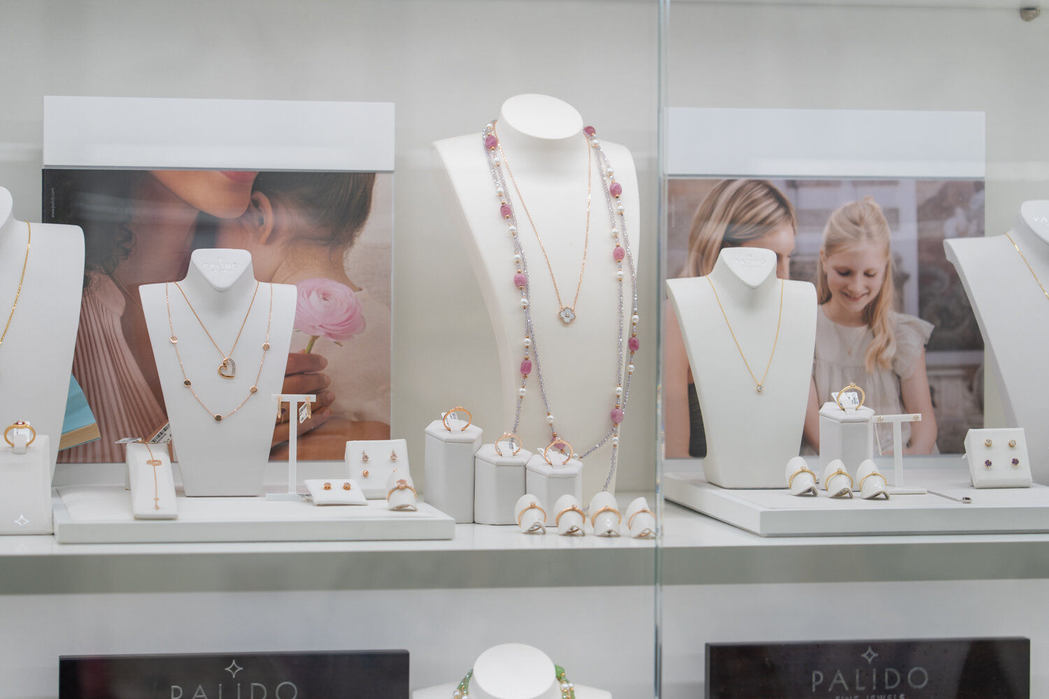 Vitrinendisplay mit filigranen Goldketten, Perlenketten und Ringen von Palido vor Werbeaufstellern.