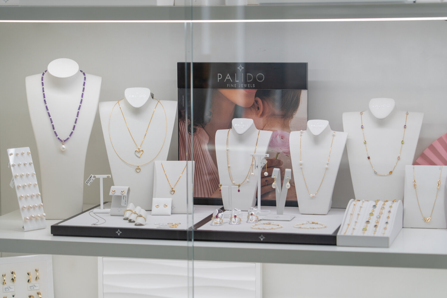 Beleuchtete Schmuckvitrine bei Juwelier Jurtschnitsch mit Palido Fine Jewels, Halsketten, Ohrringen und Ringen auf weißen Büsten.
