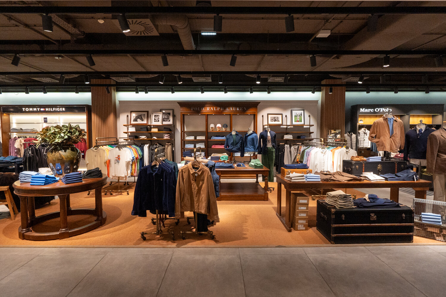 Verkaufsfläche für Herrenmode bei Kastner & Öhler mit Holzmöbeln Kleiderständern Markenbereich von Polo Ralph Lauren und braunem Teppichboden.