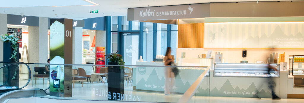Heller, moderner Verkaufsstand der Kolibri Eismanufaktur in einer oberen Etage des Kaufhaus Tyrol mit gläsernen Eisvitrinen und Sitzgelegenheiten.