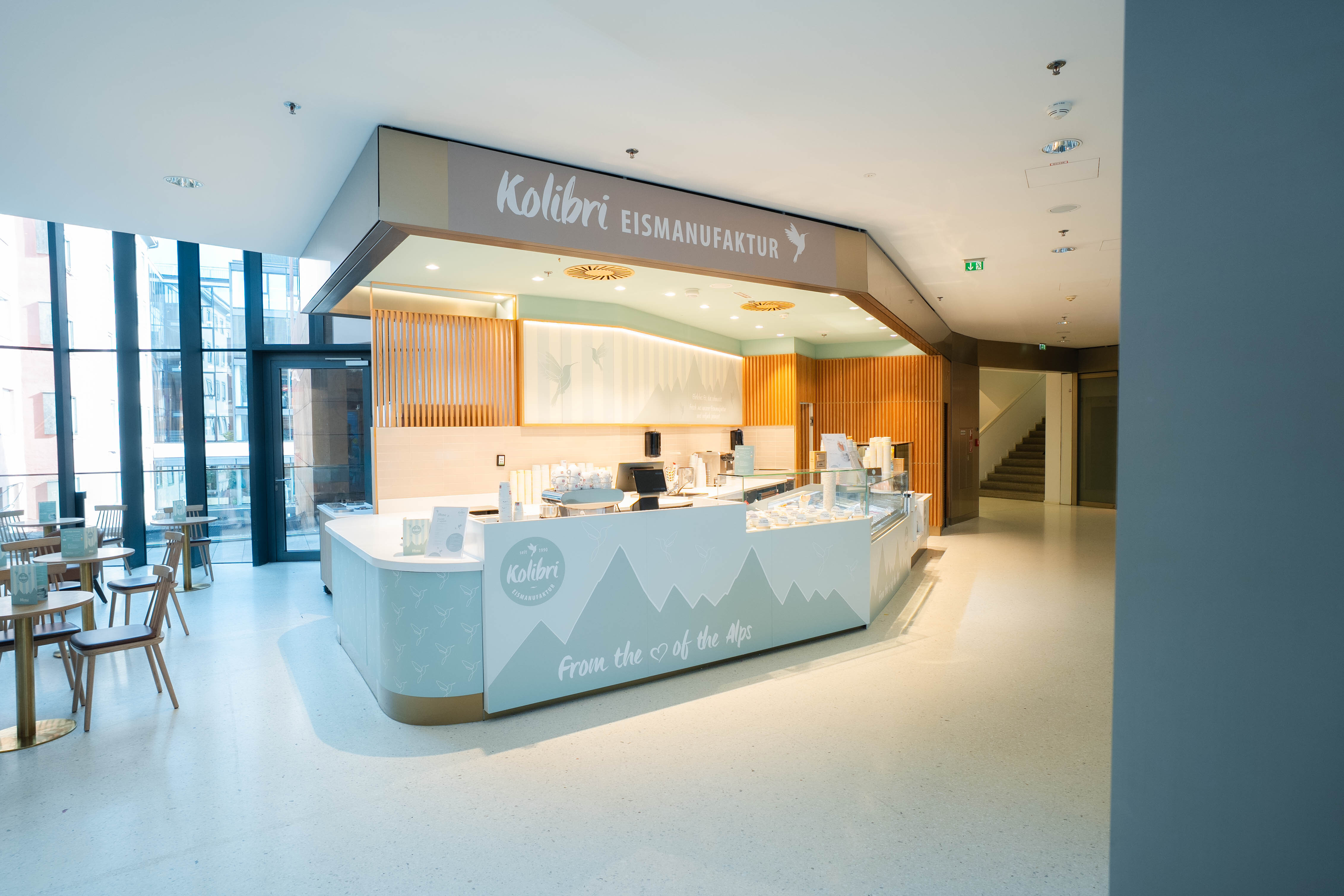 Heller Kolibri-Eisstand im Kaufhaus Tyrol mit angrenzendem Sitzbereich und großen Fensterfronten.
