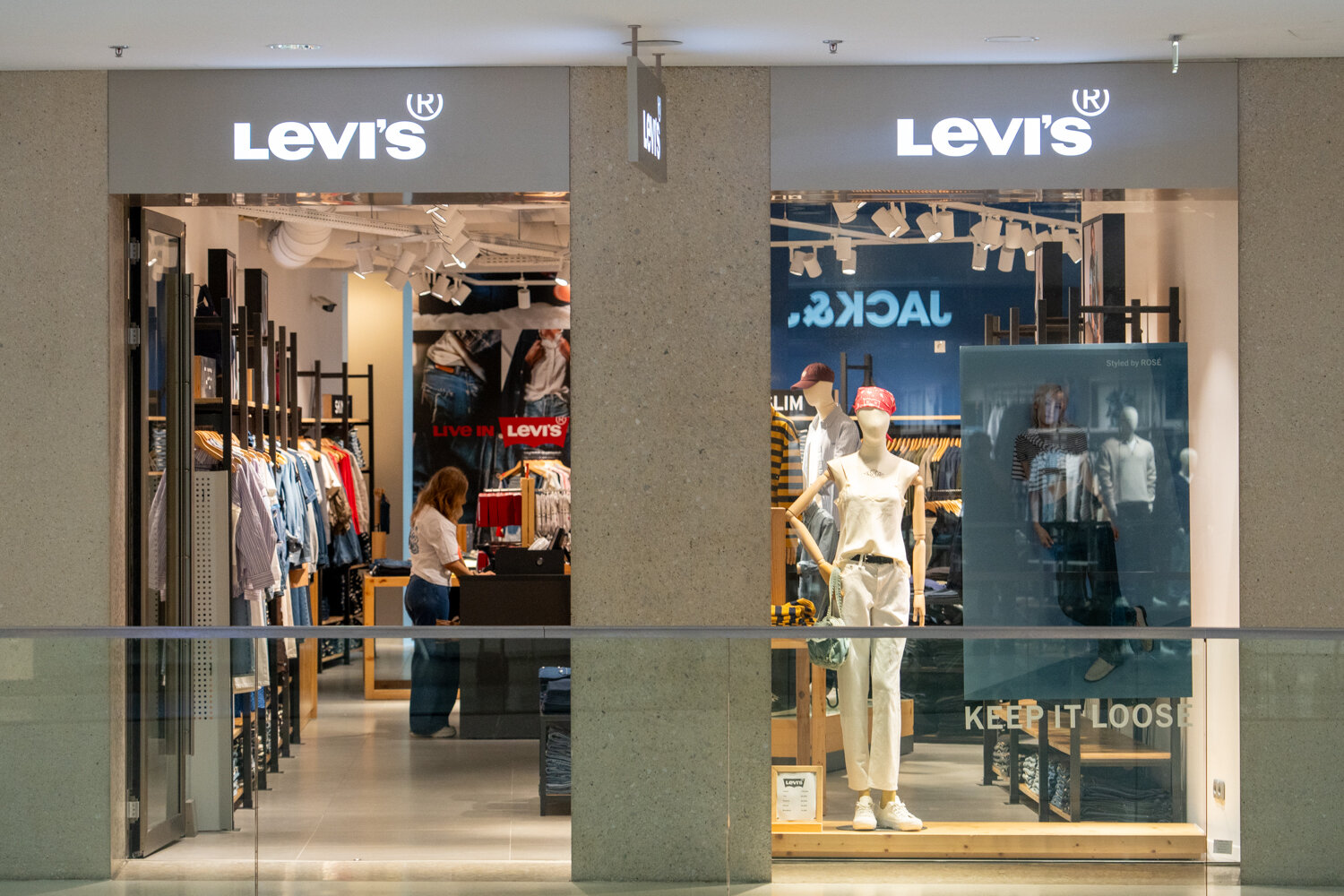 Außenansicht des Levi’s Stores im Einkaufszentrum mit beleuchtetem Logo, Schaufensterpuppen und Blick auf Verkaufsfläche und Kasse.