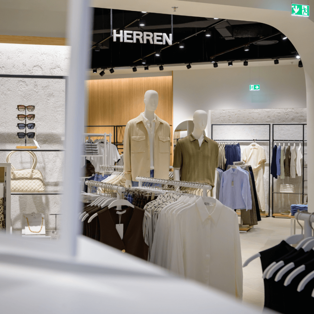 Blick in die Herrenabteilung von Mango mit Schaufensterpuppen in beigen und olivgrünen Oberteilen sowie Kleiderstangen mit Hemden.