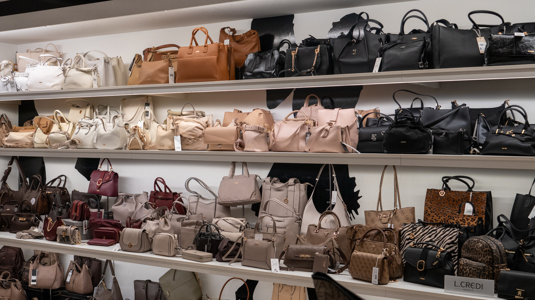 Mehrere Regaletagen bei Maniolo's bestückt mit Damenhandtaschen, Umhängetaschen und Rucksäcken in beige, schwarz, braun und Tierfell-Optik.